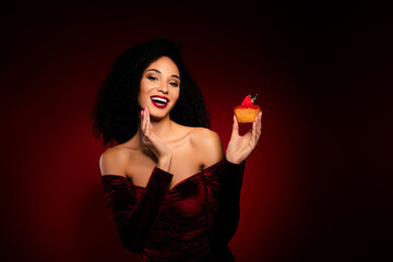 Joyful positive girl hold berry cookie biscuit enjoying smiling touch face wear velvet dress © Beauty Hero