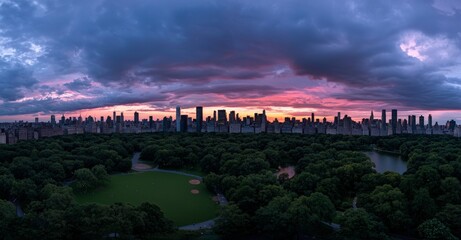 Fototapeta premium A breathtaking aerial view of Central Park features lush nature, trees, and people enjoying a picnic or resting in a field surrounded by Manhattan's cityscape and skyscrapers during a warm sunset