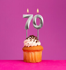 Birthday candle number 70 with cupcake on violet background.