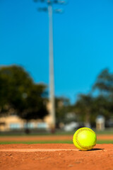 Optic yellow softball on pitcher's plate mound circle under blue sky with nobody in image