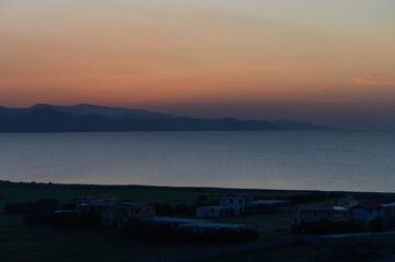 Sunset glow over tranquil waters with distant mountains and quiet coastal homes