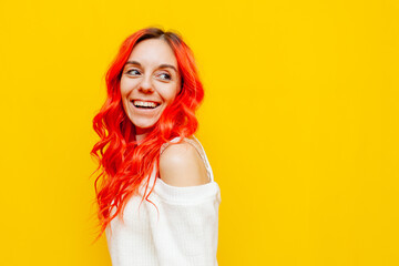 red-haired woman smiling and looking away on yellow isolated background, girl with colored curly hair looking at copy space