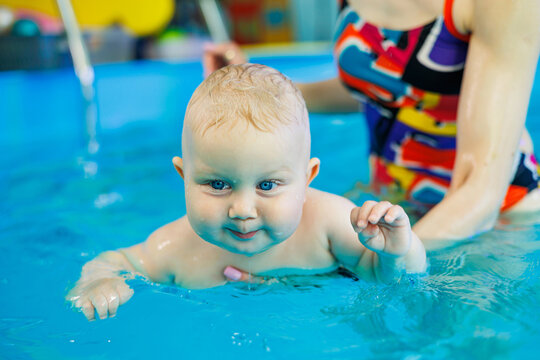 Swimming in the pool with a trainer for young children. Boy learned to swim in the water. Happy child with a woman trainer. Healthy and sporty family with a baby