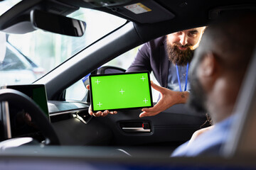 Smiling salesman using green screen tablet to present car addons options to clients, after finishing test drive. Showroom agent mockup device to husband and wife driving vehicle