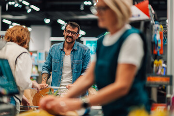 Obraz premium Smiling customer pushing shopping cart at checkout in supermarket