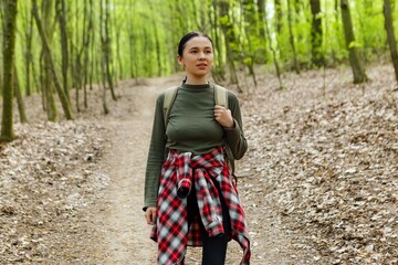 Young female hiker with a backpack walking along a winding path in the forest, savoring the fresh...