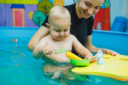 A trainer conducts a class in the pool with a baby. The child learns to swim with the trainer.