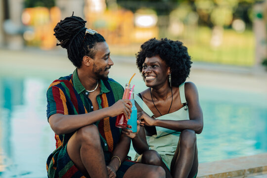 Happy couple sharing colorful drinks by the poolside