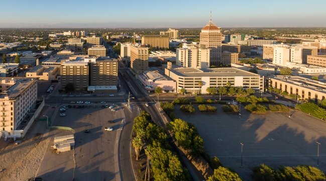 Aerial view of downtown Fresno, California, USA, at sunrise. The image shows the city's skyline, including the historic Pacific Southwest Building, and surrounding urban landscape.