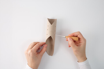 One hand is holding the tube, while the other hand is using awl to punch holes into the cardboard....