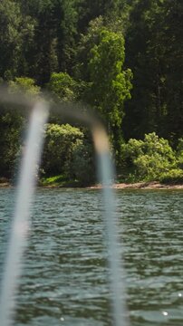 Amazing virgin forest on bank of large tranquil lake view from boat stern. Travelling by yacht to wild nature paradise on summer vacation. Water journey