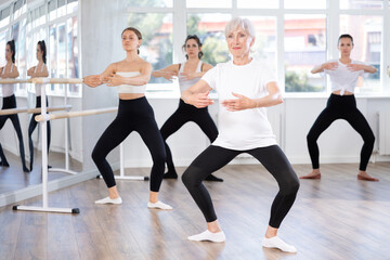 Fototapeta premium Group of slender women of different ages are learning various dance and ballet movements in the studio