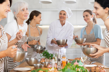 Elderly woman drinks wine and talks to group during cooking master class