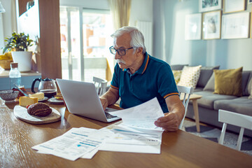 Senior man doing financials at home with laptop