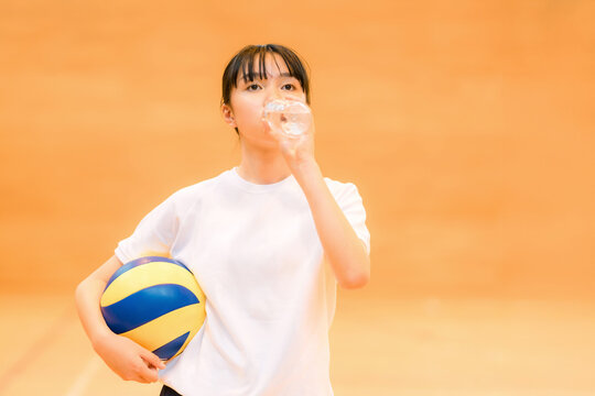 運動中に水分補給する体育館でバレーボールをする体操着姿の女子中学生・女子高生
