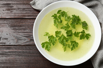 Tasty chicken bouillon in bowl on wooden table, top view. Space for text