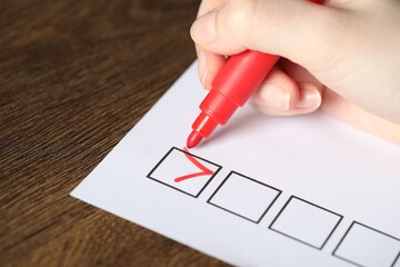 Woman checking box of paper form at wooden table, closeup
