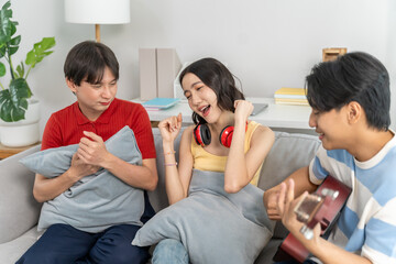 Diverse Asian friends playing guitar and dancing in living room at home.