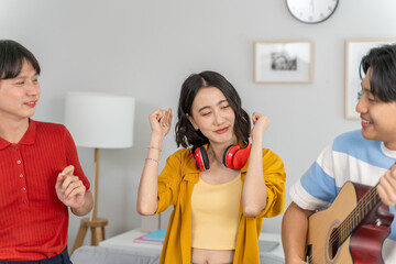 Diverse Asian friends playing guitar and dancing in living room at home.