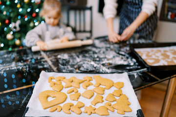 Tray of baked cookies stands on the table near a mother with a little girl making dough