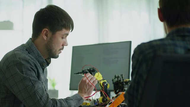 Team of programmers  concentrating on software development, writing code of robotics arm and analyzing data on a computer.