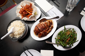 Three flavorful Chinese dishes served together for a perfect feast, stir fried string beans with minced pork, crispy basket with savory shredded pork, and roasted duck with caramelized glaze.