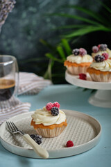 Cupcakes with vanilla cream and berries. Blue background, side view