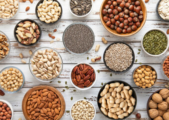 Mixed assorted raw healthy nuts and seeds in various bowls on light wooden table.Peanut,hazelnut,walnut,almonds,pistachio,sunflower,pumpkin,chia and cashew.Top view.
