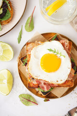 Delicious sandwich with fried egg and bacon on light background