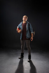 person stands confidently wearing a denim jacket over a maroon sweater, holding a blue jacket in a...
