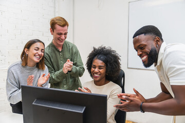 Happy business team clapping celebrating success at computer in coworking office