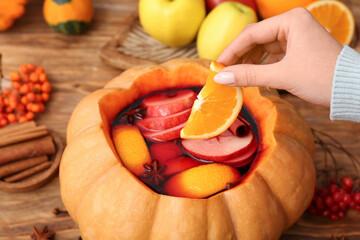 Woman preparing tasty mulled wine in pumpkin on wooden background