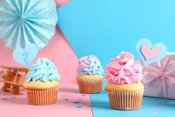 Delicious cupcakes with gift box, decorations and toy on color background. Gender reveal party concept