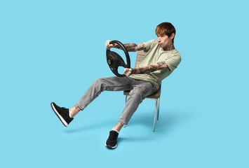 Emotional young man with steering wheel on blue background