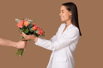 Young woman receiving bouquet of beautiful flowers on brown background