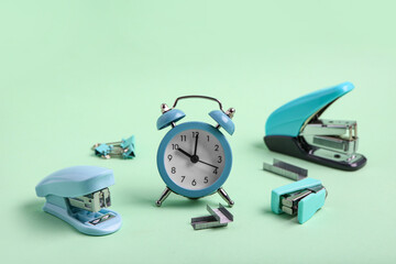 Blue staplers with staples and alarm clock on green background