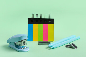 Blue stapler with staples, pens and bookmarks on green background