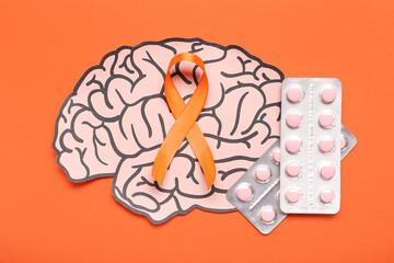 Paper brain with pills and orange ribbon on color background. Multiple Sclerosis Awareness Month