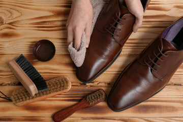 Hands cleaning shoes with cloth on wooden background