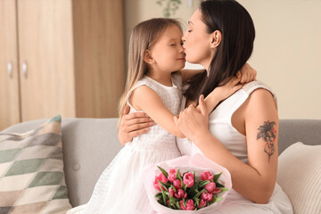 Happy mother kissing her cute little daughter at home on holiday