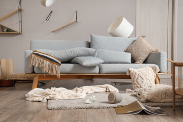 Sofa with overturned things on carpet in messy living room
