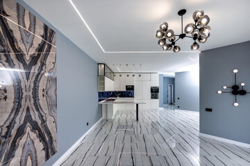 A large open living room with a white kitchen and a black chandelier hanging from the ceiling
