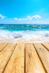 Fototapeta premium Sunny beach scene with wooden planks in foreground, ocean waves crashing on sandy shore under bright blue sky