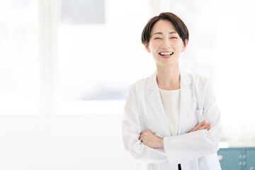 白衣を着たミドル世代の女性が腕組みをしている。