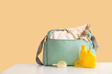 Baby bag with bottles of cream on table against beige background