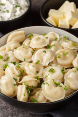 Russian pelmeni dumplings with sour cream, butter and herbs close-up on the table. Vertical