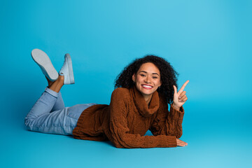Young woman in casual clothing smiling and pointing enthusiastically against a bright blue backdrop