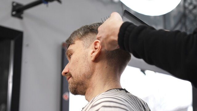 Professional barber carefully combing client's hair, preparing precise haircut in stylish barbershop, delivering contemporary men's grooming service
