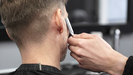 Professional barber carefully shaving client's beard, gripping straight razor with expertise while working in classic barbershop setting