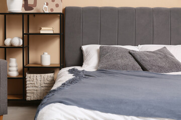 Comfortable bed with pillows and shelving unit in interior of stylish bedroom